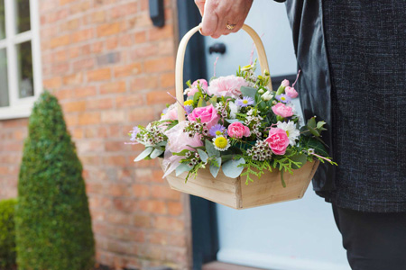 Hand holding a basket of pink and pastel spring flowers outside a home