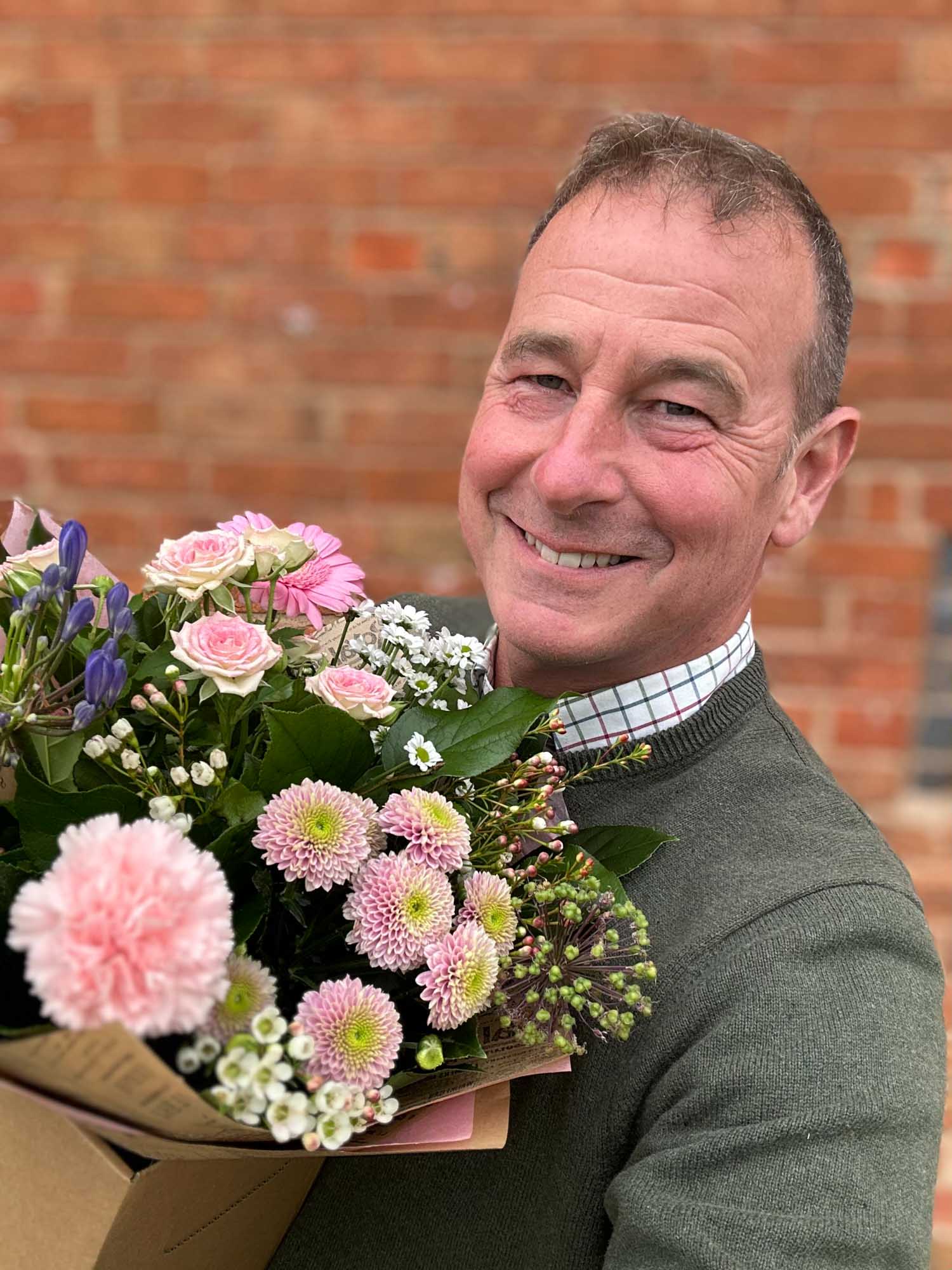 Selfie of a middle-aged man smiling hugging a box of flowers.