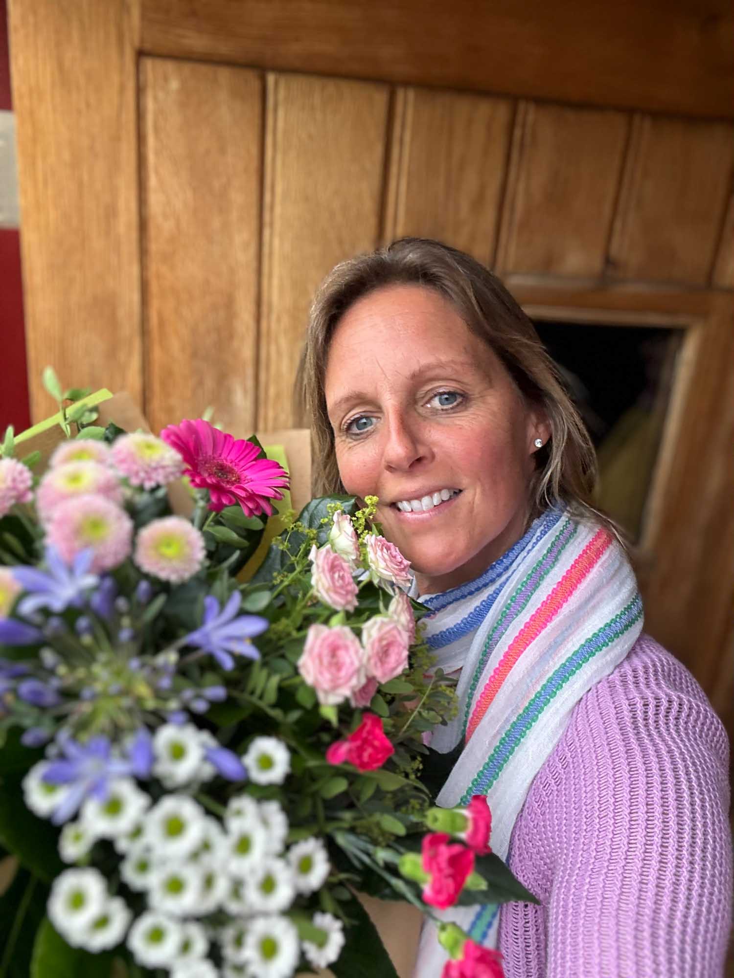 Selfie of a woman at front door smiling and hugging a vibrant delivery of flowers.