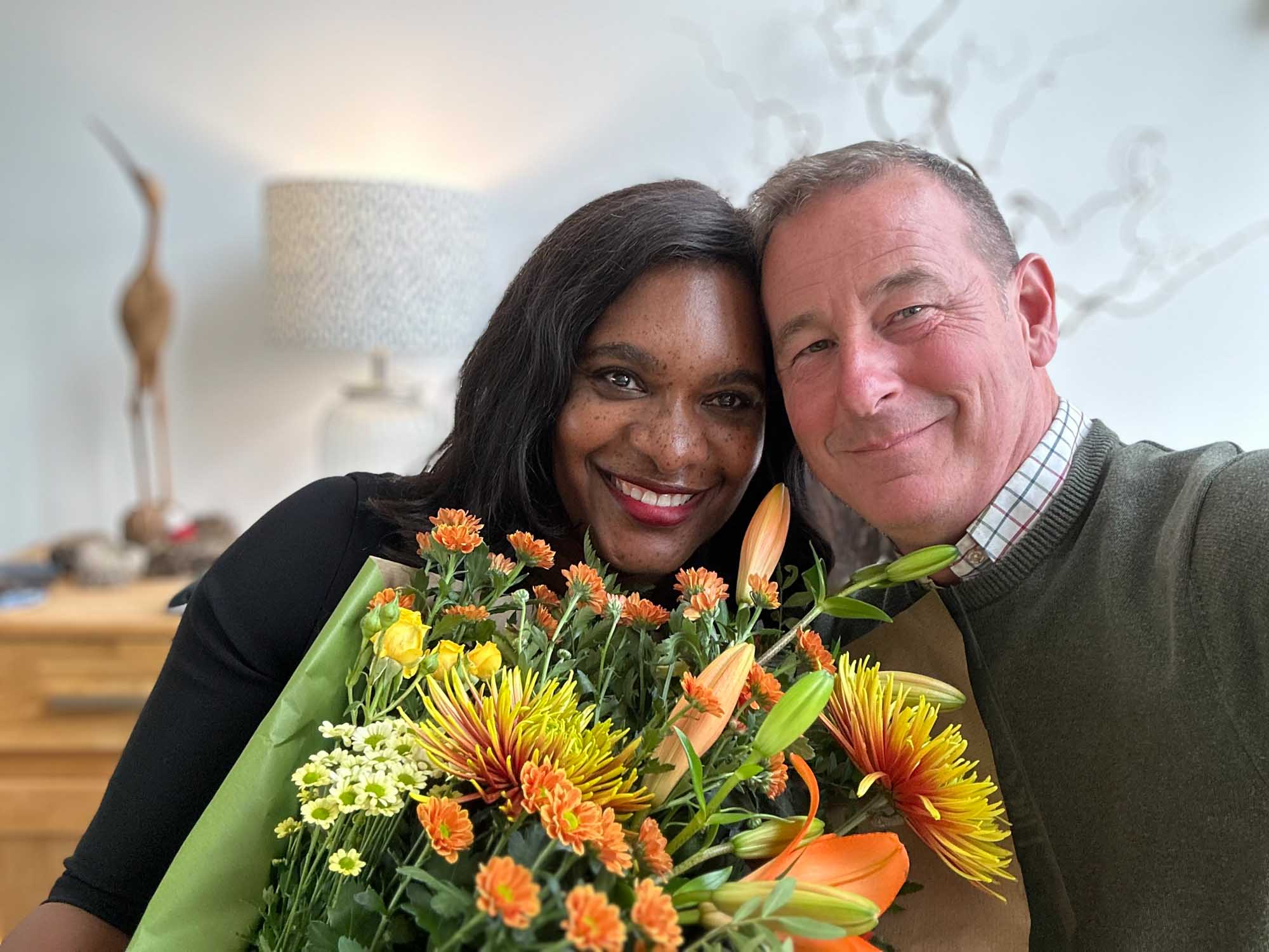 Smiling mixed race couple close together holding a vibrant yellow and orange wrap