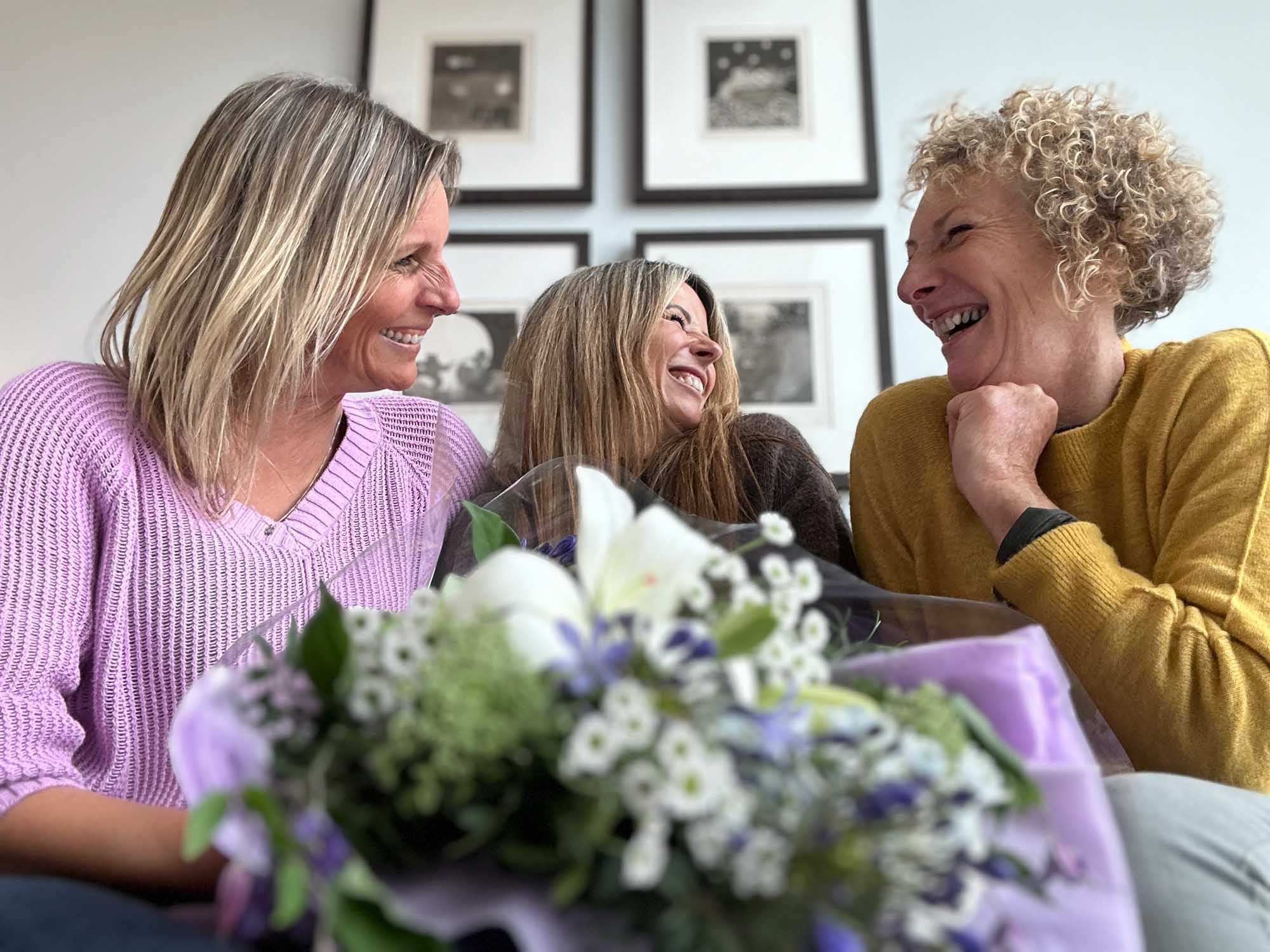 group of 3 friends laughing and enjoying each others company with a featured lilac gift wrap layed on a table in front of them