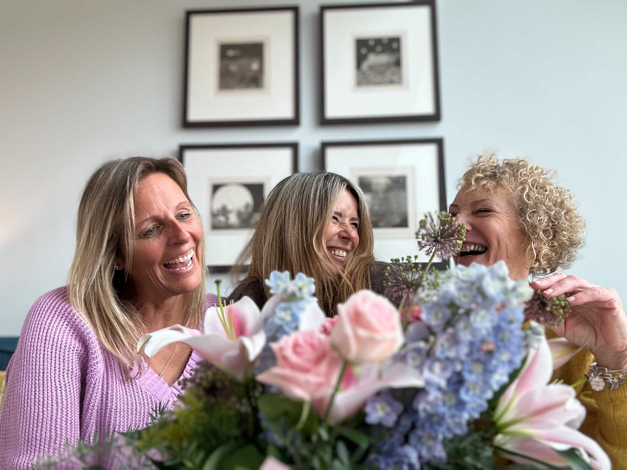 Pink bouquet delivery in foreground with three friends laughing